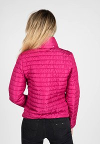Giacca rosa gonfiabile con design trapuntato, colletto alto e dettagli di cucitura visibili, abbinata a jeans neri.