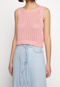 Haut en tricot rose sans manches avec une texture côtelée et des mailles ouvertes, associé à une jupe en denim bleu clair avec une taille à cordon.