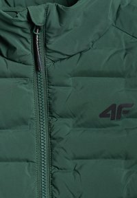 Veste matelassée vert foncé avec une fermeture éclair à l'avant et un logo 4F noir sur le côté droit.