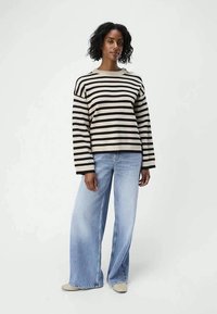 Gestreepte trui in beige en zwart, met een brede halslijn en lange mouwen. Gecombineerd met lichtblauwe wijde jeans.