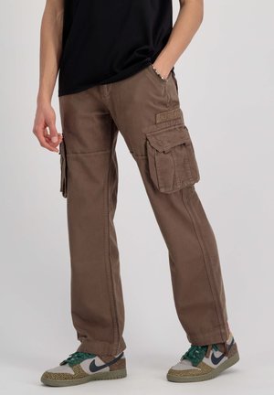 Brune cargo bukser lavet af bomuld, med flere sidelommer og en afslappet pasform. Båret med mønstrede sneakers og en sort top.