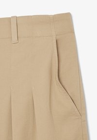 Pantaloni in cotone beige con tasche laterali, caratterizzati da una parte frontale piatta, pieghe e passanti per cintura, che mettono in risalto una finitura liscia e texturizzata.