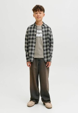 Zwart-wit geruite flanellen shirt over een grijze graphic tee, gecombineerd met losse, donkergrijze broek en lichtbeige instappers.