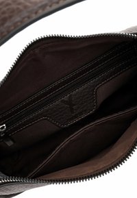 Sisäkuva ruskeasta nahkalaukusta, jossa on useita lokeroita, mukaan lukien vetoketjullinen tasku ja kangasvuori.