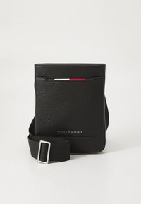 Black leather messenger bag with a textured finish, flap front, adjustable strap, and a red, white, and blue accent stripe. Logo on front.