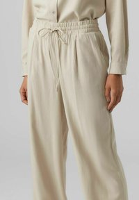 Pantalons beige à enfiler avec une taille élastique et un cordon de serrage ajustable. Le tissu est doux avec une finition texturée et une coupe décontractée.