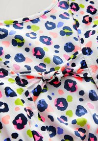 Tissu blanc avec un motif léopard éclatant en bleu marine, rose, vert et violet, avec un détail noué au niveau du col. Texture lisse.