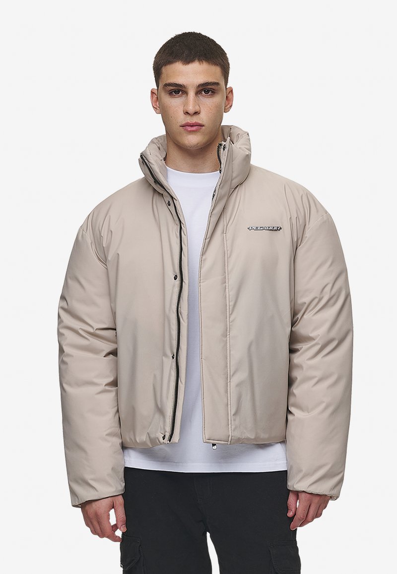Jachetă puffer izolată bej, cu guler înalt, fermoar frontal și accent cu logo. Are o textură netedă și lucioasă, precum și o croială lejeră.