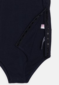 Mornarski bodysuit s mekanom teksturom, sa zatvaranjem na dugmad uz jednu stranu u crnoj boji i oznakom koja je vidljiva blizu šava.