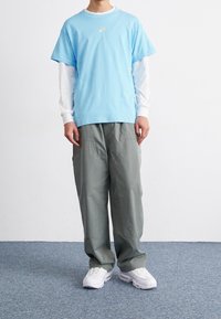 Ljusblå t-shirt med kort ärm över en vit långärmad skjorta, kombinerad med lösa grå cargobyxor och vita träningsskor.