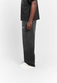 Gray oversized t-shirt, relaxed-fit black sweatpants with white logo, paired with white sneakers. Soft texture, straight leg, minimal design.