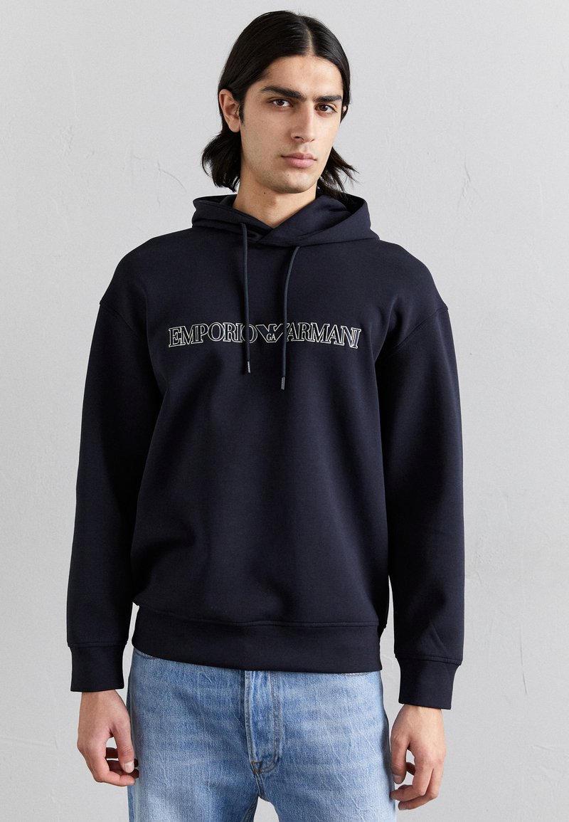 Felpa navy con stampa del logo sul fronte, cappuccio con cordino e polsini a costine. Abbinata a jeans denim azzurri, per un look casual.