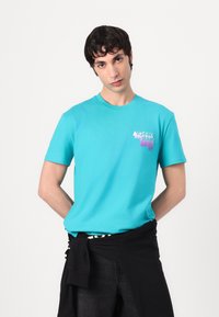 Tyrkysové bavlněné tričko s krátkými rukávy a kulatým výstřihem. Obsahuje barevné logo na hrudi a má volný střih.