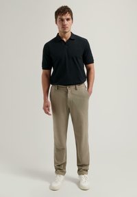 Svart polo-skjorte og beige chinos med rett snitt. Bært med hvite sneakers. Enkelt design, ingen synlige mønstre eller logoer.