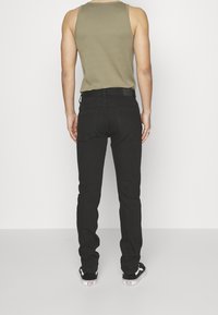 Jeans de mezclilla negros con un corte ajustado, que cuentan con bolsillos traseros y un acabado texturizado, combinados con una camiseta de tirantes gris y zapatillas negras.