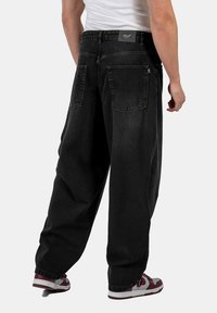 Pantalones de mezclilla negros de corte holgado, con dos bolsillos traseros, costuras mínimas y una pequeña etiqueta en la cinturilla.