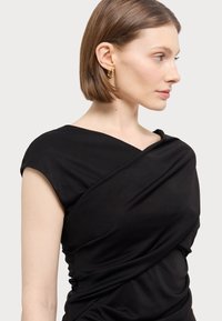 Zwarte wikkeljurk met korte mouwen, gemaakt van gladde stof. Kenmerkt zich door gedrapeerde details op het lijfje. Eenvoudig ontwerp, zonder zichtbare patronen of accenten.