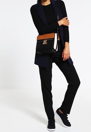 Crossbody taske med en sort stofkrop, top i tan læder, guldfarvede detaljer og en struktureret rektangulær form.