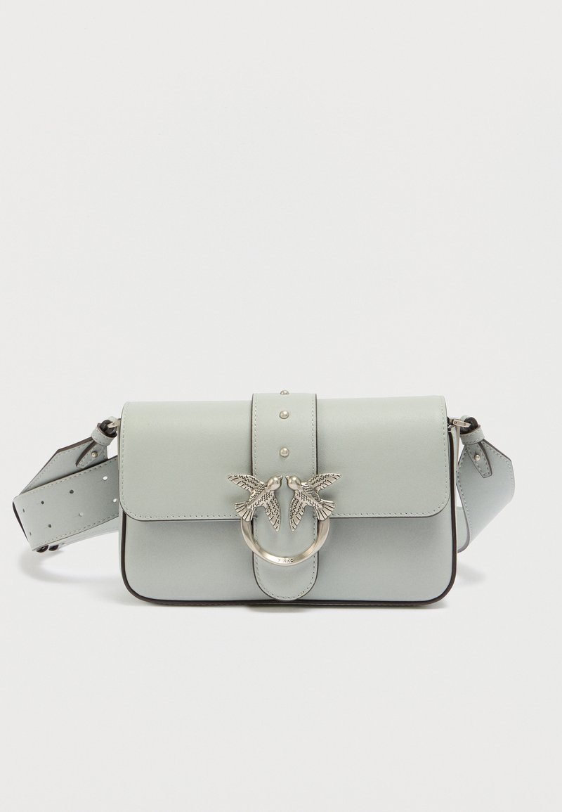 Τσάντα χειρός από ανοιχτό μπλε δέρμα με καπάκι, ασημένιες διακοσμήσεις σε σχήμα πουλιού και λεπτομέρειες με τρουκς. Περιλαμβάνει αποσπώμενο λουρί με ρυθμιζόμενο μήκος.