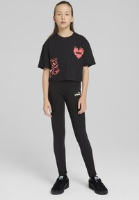 Černé zkrácené tričko s růžovou zvířecí grafikou a logem, spárované s černými legínami s logem. Černé tenisky dokončují outfit.