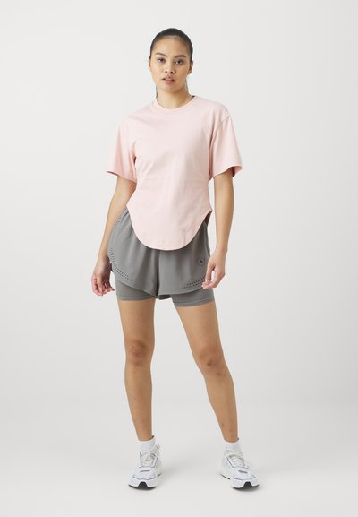 Lys rosa bomull T-skjorte med korte ermer og buet hem, kombinert med grå treningsshorts med perforerte detaljer og spandex-fôr.