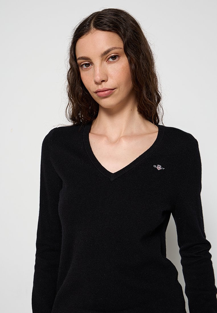 Schwarzer V-Ausschnitt-Pullover aus weichem Stoff, mit langen Ärmeln und kleinem Logo auf der linken Brustseite. Glatter Stoff und taillierte Passform.