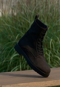 Stivaletti in suede neri alla caviglia con lacci frontali, punta tonda e suola in gomma resistente. Presentano un piccolo passante sul retro per una facile calzata.