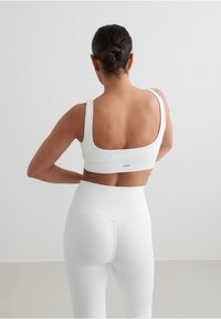 Hvit ribbet crop top og high-waisted leggings med brede stropper og jevn finish. Merkevarelogoen er synlig på baksiden av toppen.