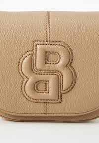 Borsa in pelle color cuoio con logo impresso e superficie testurizzata. Presenta accenti cuciti e una chiusura a patta, che mette in mostra un design elegante e compatto.