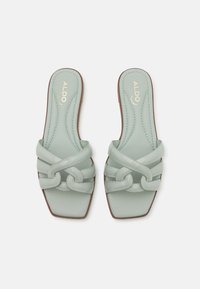 Sandales à glissière vert menthe avec un design de lanières croisées, bout carré et semelle plate. Texture lisse avec des détails de surpiqûres subtiles.