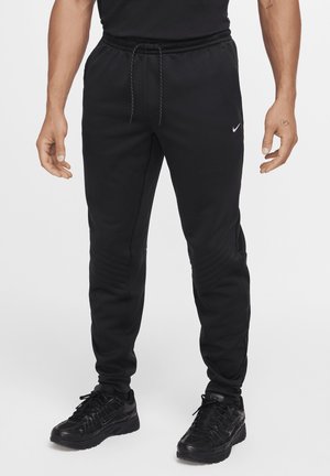 Black athletic pants with a drawstring waist. Features ribbed texture along the sides and a small logo on the left leg. Made of soft material.