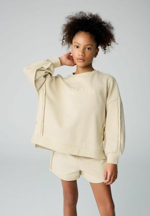 Felpa beige over-size con spalle cadenti, polsini a coste e logo sottile. Abbinata a degli shorts fitted dello stesso colore.