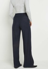 Granatowe spodnie o szerokich nogawkach, wykonane z miękkiego materiału, z dopasowanym pasem i plisowanymi detalami, zestawione z dopasowaną szaro-skalową bluzką i czarnymi balerinami.