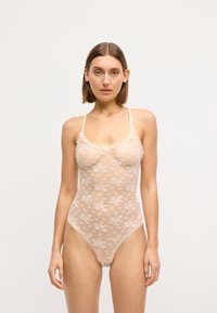 Body z koronką w kolorze nude, z kwiatowym wzorem, delikatnymi falbankami wzdłuż dekoltu i cienkimi, regulowanymi ramiączkami.