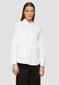 Weißes Hemd mit Knöpfen, Kragen und langen Ärmeln. Mit tonal gesticktem Design auf der linken Seite. Glattes Material, taillierte Passform.