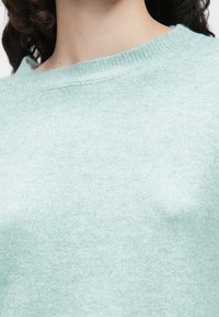 Lys mintgrønn strikkegenser med myk tekstur, med bred halsringning og ribbestrikket krage. Minimalistisk design uten synlige mønstre.