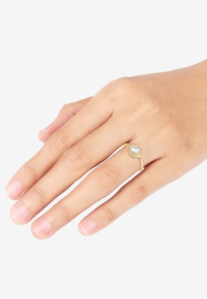Guldring med en cirkulær, opalescent sten omgivet af små klare ædelsten, sat på en glat, slank ring.