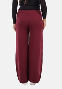 Pantaloni a gamba larga color bordeaux realizzati in tessuto morbido, caratterizzati da vita alta, cuciture laterali e un design fluido. Texture liscia e senza motivi visibili.