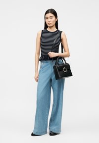 Frau trägt ärmelloses, marineblau gestreiftes Oberteil, hoch taillierte, weit geschnittene Jeans und hält eine schwarze Handtasche mit goldenem Ringdetail.