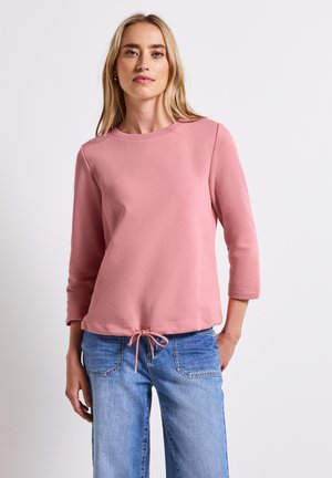 Heller rosa Pullover mit rundem Ausschnitt, drei Viertelärmeln und einem Tunnelzug am Saum. Weicher, strukturierter Stoff. Kombiniert mit Denim.