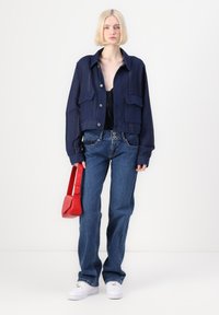 Ναυτικό μπλε κοντό μπουφάν με δύο μπροστινές τσέπες και κουμπιά, συνδυασμένο με ανοιχτό μπλε ίσια τζιν παντελόνια. Κόκκινη τσάντα και λευκά αθλητικά παπούτσια.