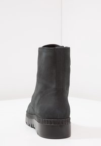 Sort ankelstøvle lavet af glat læder, med en tekstureret sål og en let hæl. Har minimal syning og et strømlinet, moderne design.