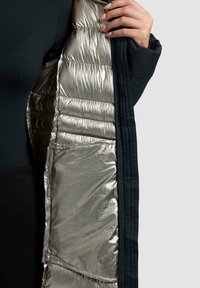 Črna zunanja jakna z metalno srebrno podlogo, ki ima polnjeno izolacijo in eleganten videz. Vidna stranska žep.