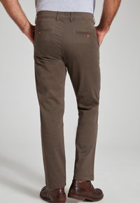 Khaki cotton trousers with a slim fit, featuring two back pockets with brown buttons, and a smooth texture. Worn with brown leather shoes.