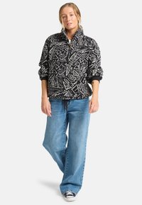 Sorte og hvite mønstrede fleece-pullover med halv-zip krage, kombinert med lyseblå vide jeans og svarte joggesko.