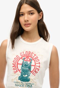Camiseta sin mangas blanca con un gráfico colorido de un Buda riendo, con texto rojo y turquesa a su alrededor, en una textura de algodón suave.