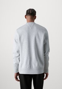 Grå sweatshirt med ribbet halsudskæring og manchetter, præget af en subtil tekstur. Bagfra ses en v-formet stikning detalje ved kraven.