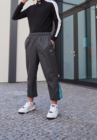 Czarna bluzka z długim rękawem i białymi paskami, zestawiona z szarymi, kratkowymi spodniami o długości do kostek, z turkusowym zamkiem bocznym i logo. Białe buty sportowe.