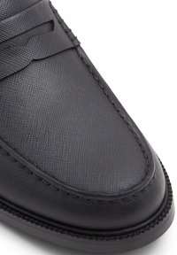Zapato de cuero negro con un acabado texturizado, punta redondeada y costuras decorativas a lo largo de los bordes. Diseñado con una silueta sin cordones.