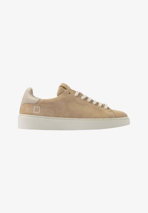 Beige suède lage sneaker met witte veters, witte zool en gevoerde hielkraag, zijbranding met ingebossing en gestikt vierkant logo nabij de hiel.